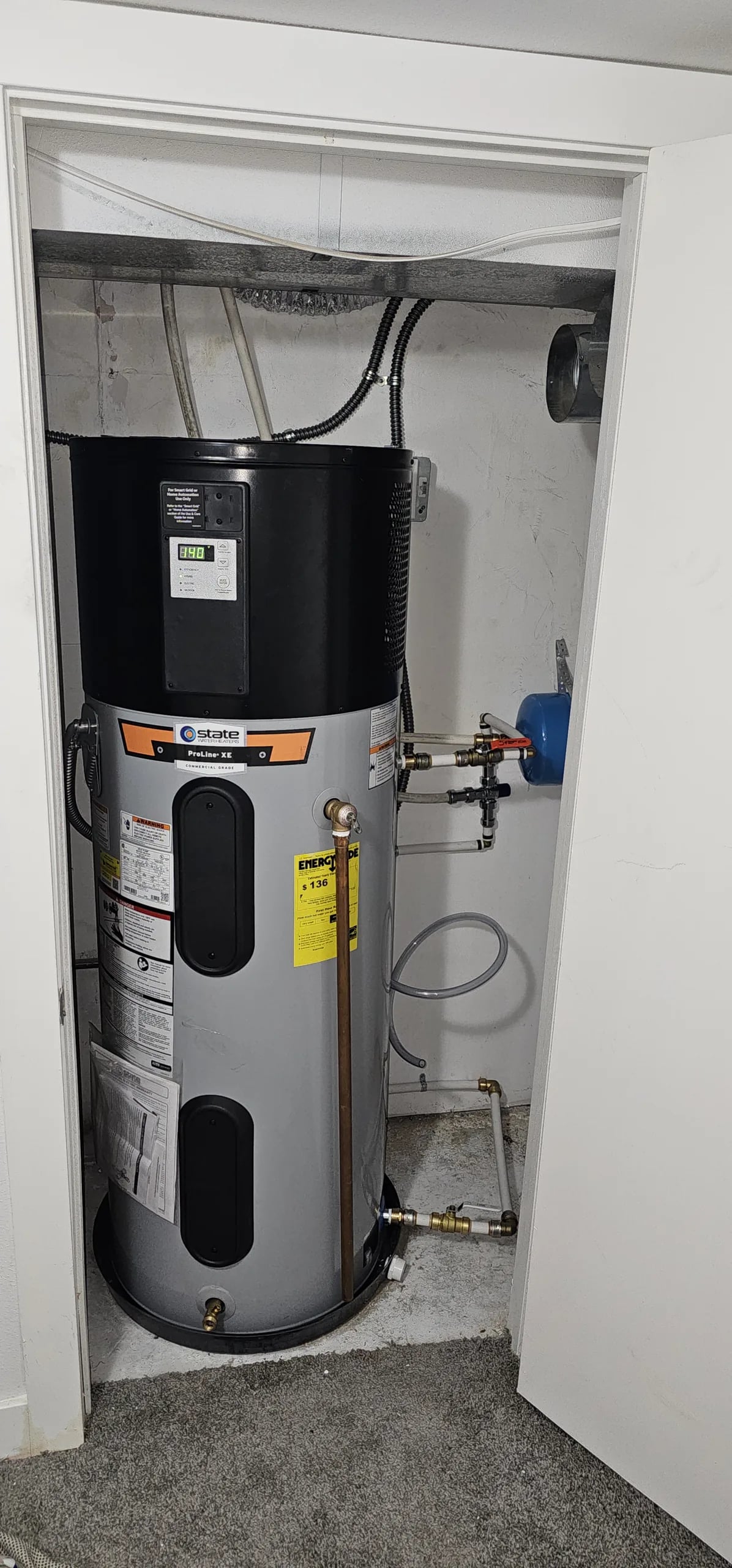 Heat pump water heater in a closet, with its compressor and fan housing on top of the tank